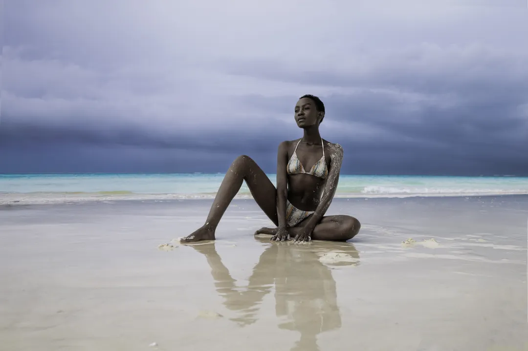 Editoriale beachwear costruito attorno a un cielo in tempesta — il rischio meteo diventato scenografia.